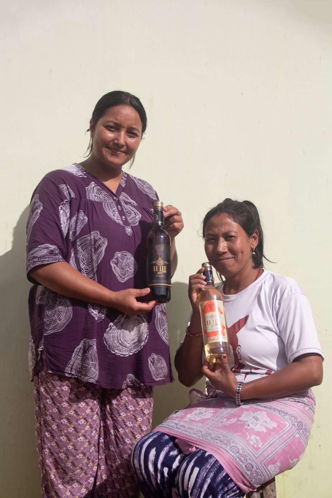 Two women of Le Le holding the red and white bottles