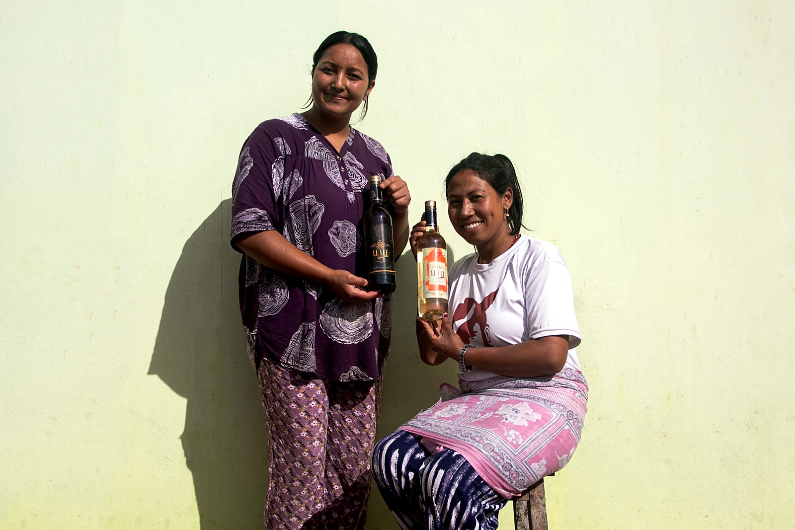Two makers of Le Le seated together, each holding a bottle